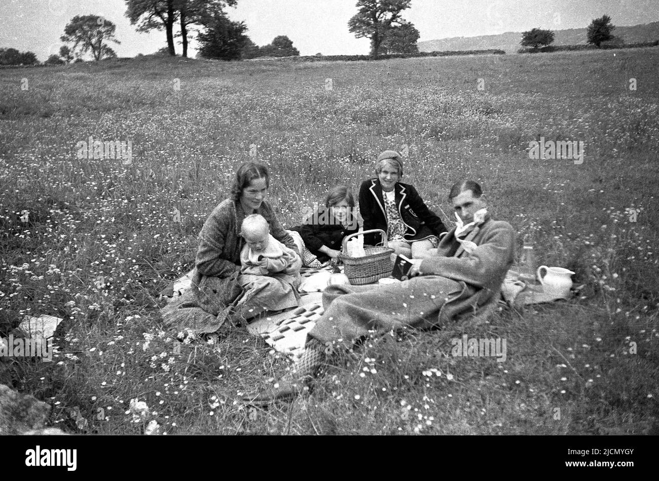 1950s, historisches Familienpicknick auf einem Feld, Vater, Mutter, kleine Kinder und Neugeborene sitzen auf einem Teppich auf dem Gras, England, Großbritannien. Stockfoto