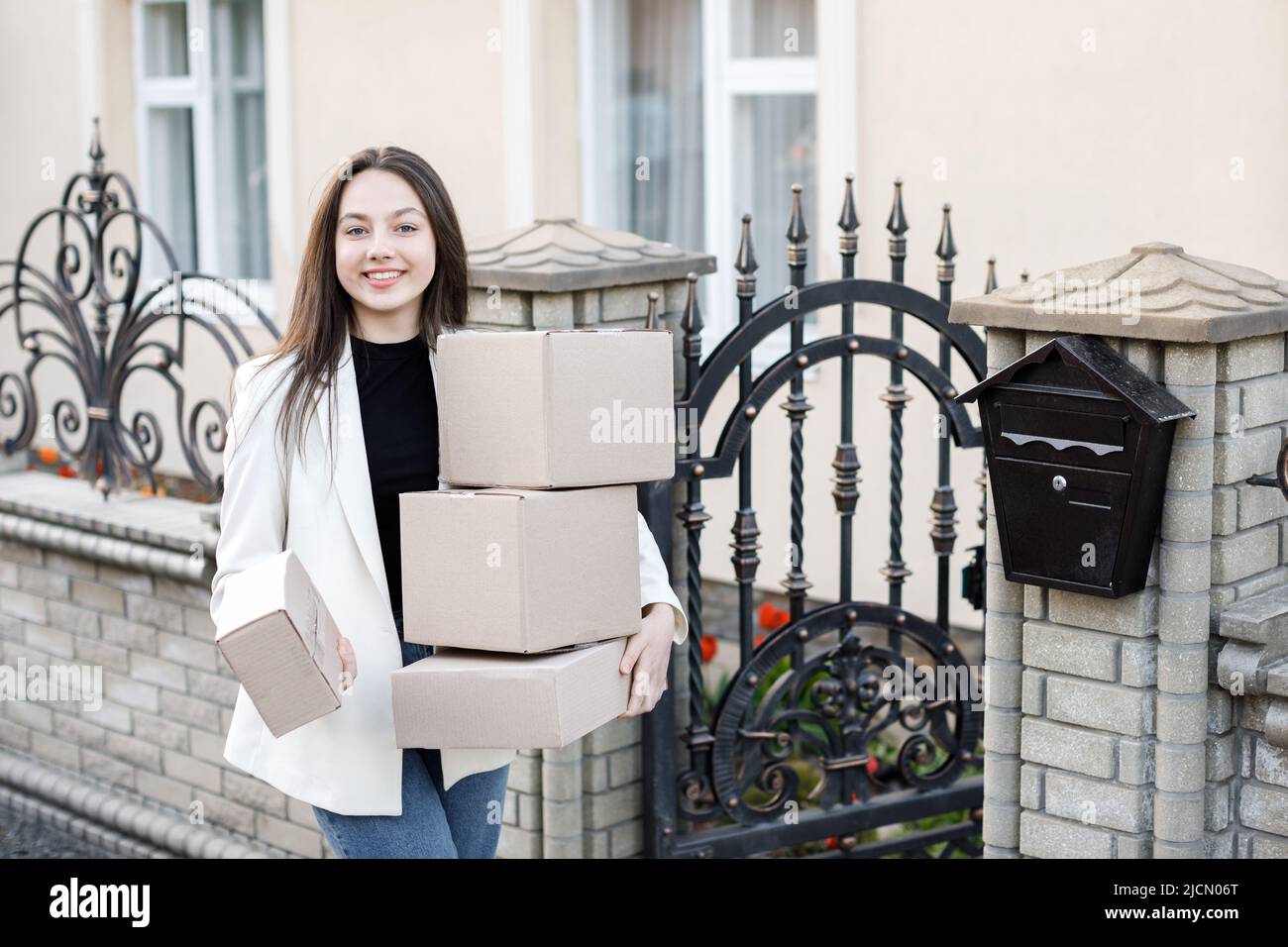 Junge Frau, die Pakete nach Hause trägt und mit einem Haufen Pappkartons steht. Stockfoto