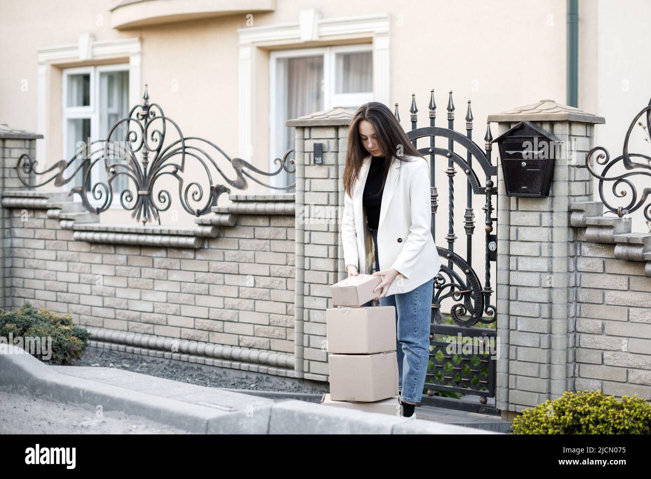 Junge Frau, die Pakete nach Hause trägt und mit einem Haufen Pappkartons steht. Stockfoto
