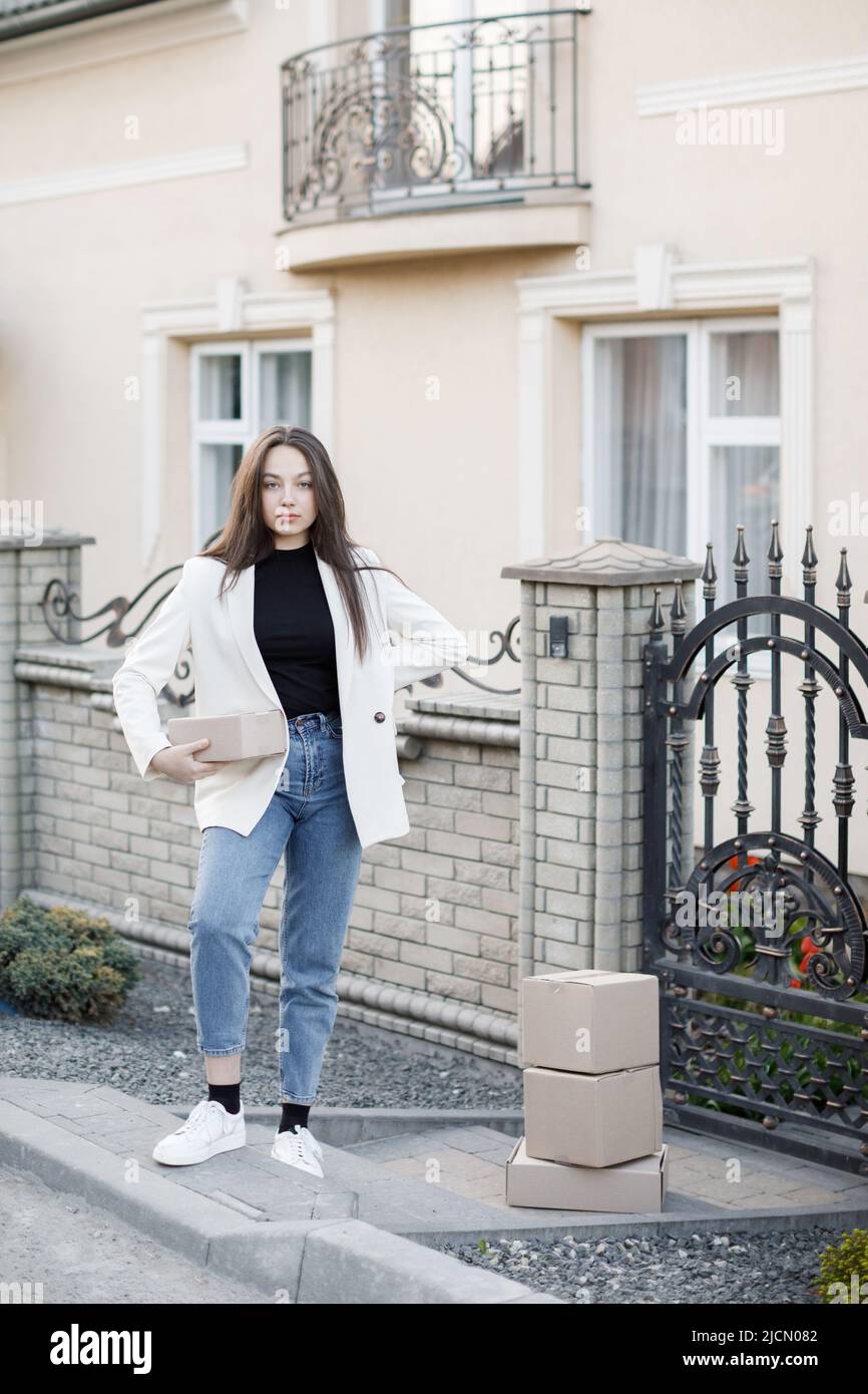 Junge Frau, die Pakete nach Hause trägt und mit einem Haufen Pappkartons steht. Stockfoto