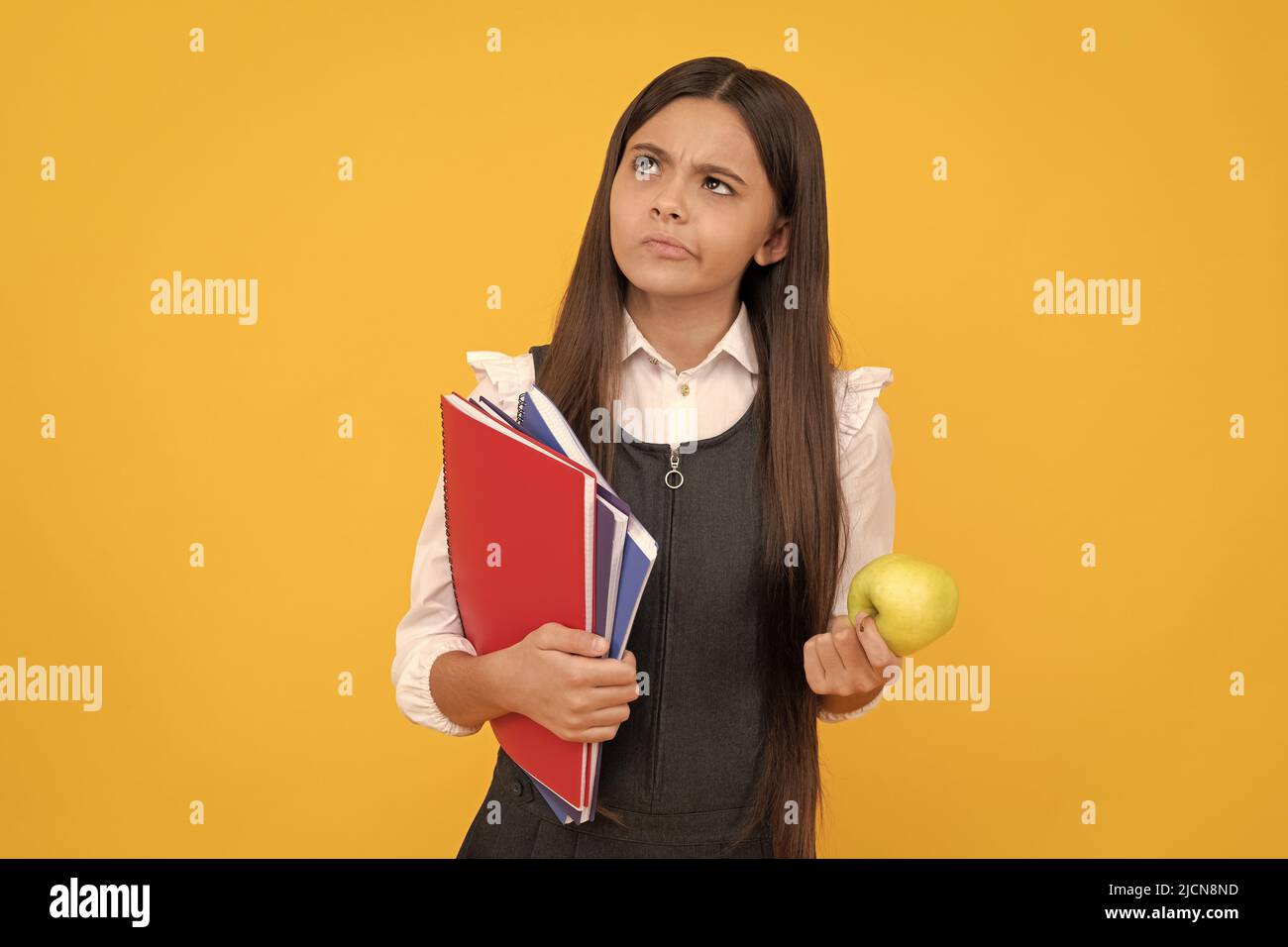 Ernst Mädchen im schulpflichten Alter Kind denken, hält Apfel und Bücher gelben Hintergrund, denken Stockfoto