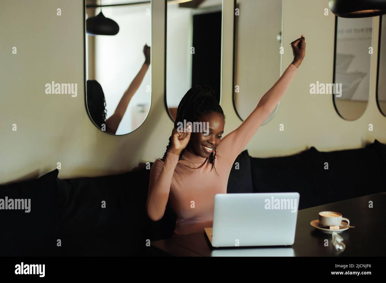 Froh erfolgreiche und stolze interracial afro amerikanische Geschäftsfrau auf Remote-Arbeit im Café. Den Arm heben, den Sieg Stockfoto