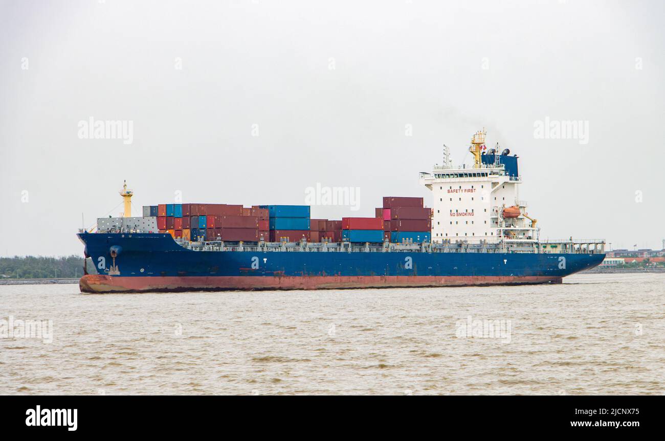 Das Containerschiff, das mit Containern beladen ist, segelt an einer Küste entlang Stockfoto