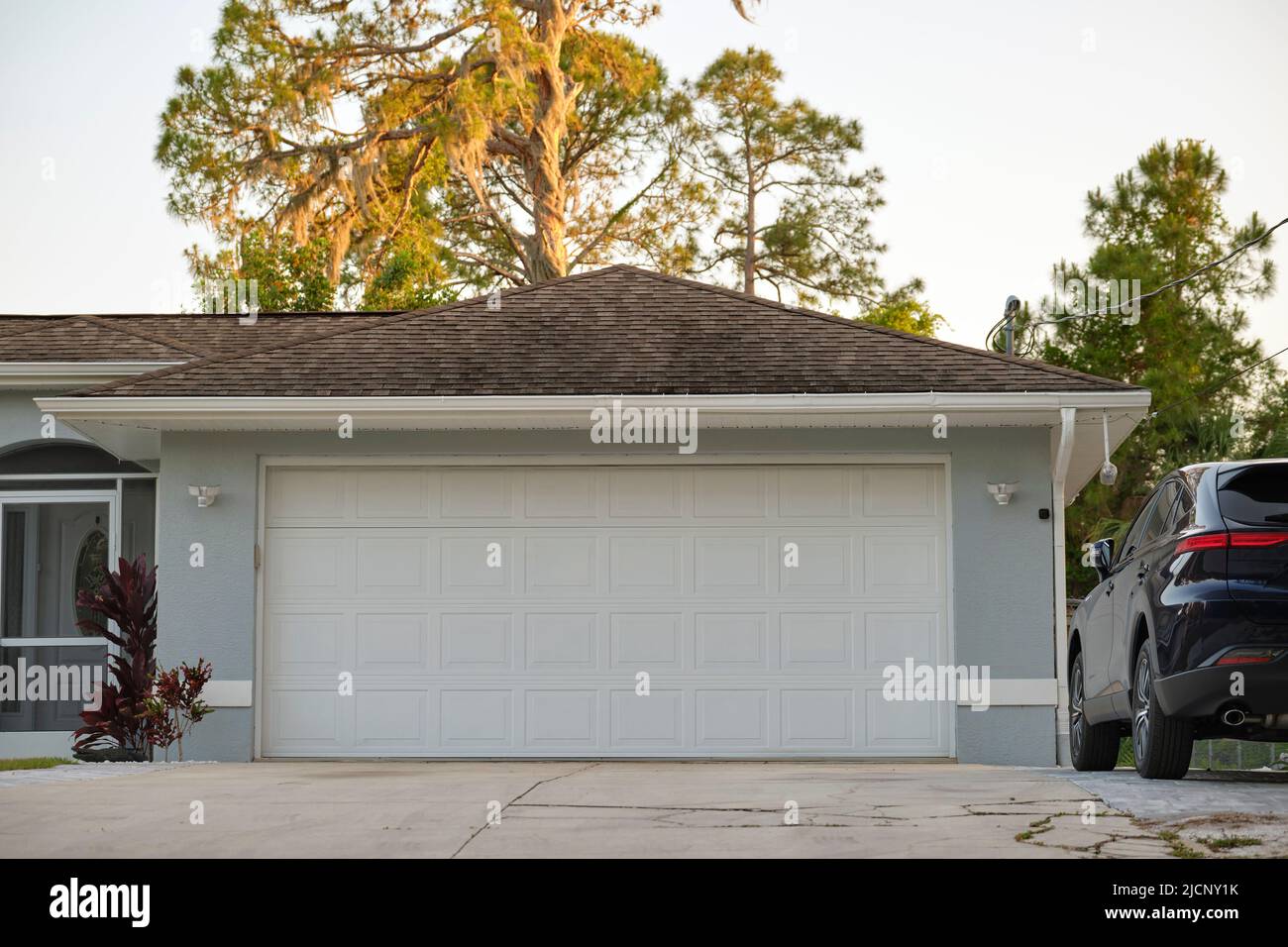 Das Auto parkte vor dem breiten Doppeltor der Garage auf der Betoneinfahrt des neuen modernen amerikanischen Hauses Stockfoto