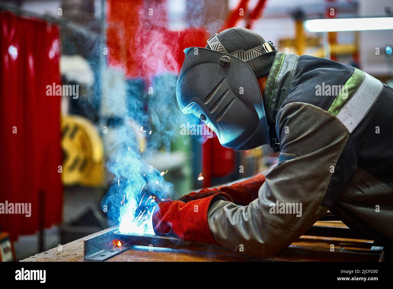 Facharbeiter in der Schutzmaske schweißt Metallteile im Werk Stockfoto