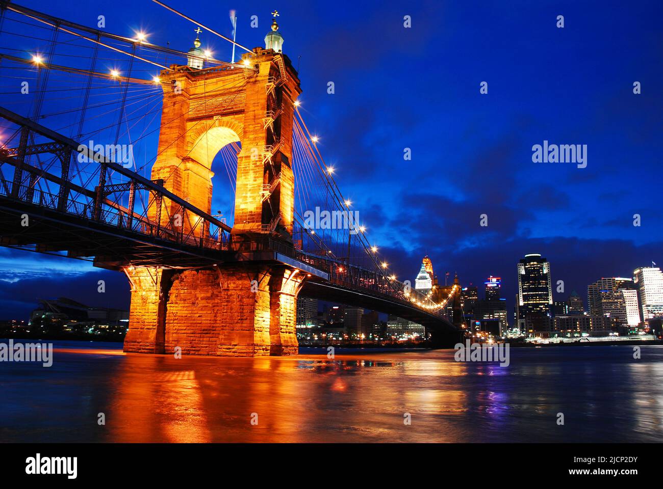 Die Lichter der Skyline von Cincinnati und der Roebling Bridge spiegeln sich nachts im Wasser des Ohio River wider Stockfoto
