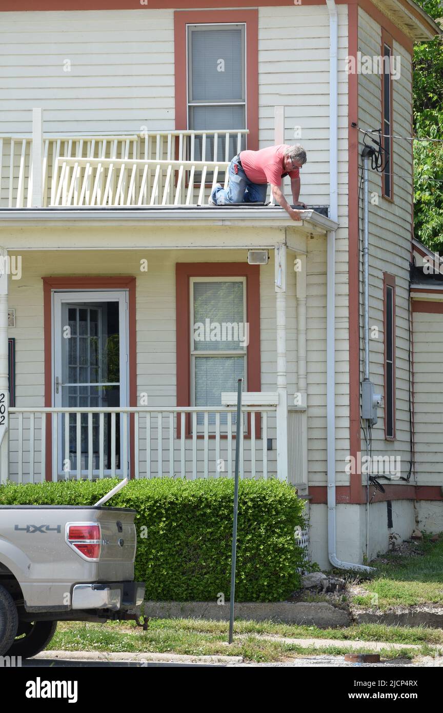 Ein Handwerker kniete auf und arbeitete auf einem Dach eines Hauses Stockfoto