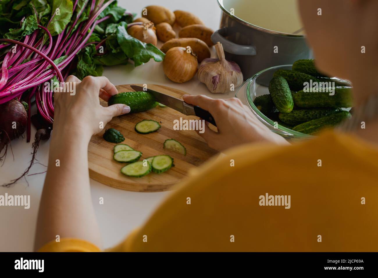 Weibliche Hände schneiden Gurken auf Holz Schneidebrett in der Küche, ein Stück Essen. Gesunde Ernährung. Über der Schulter Stockfoto