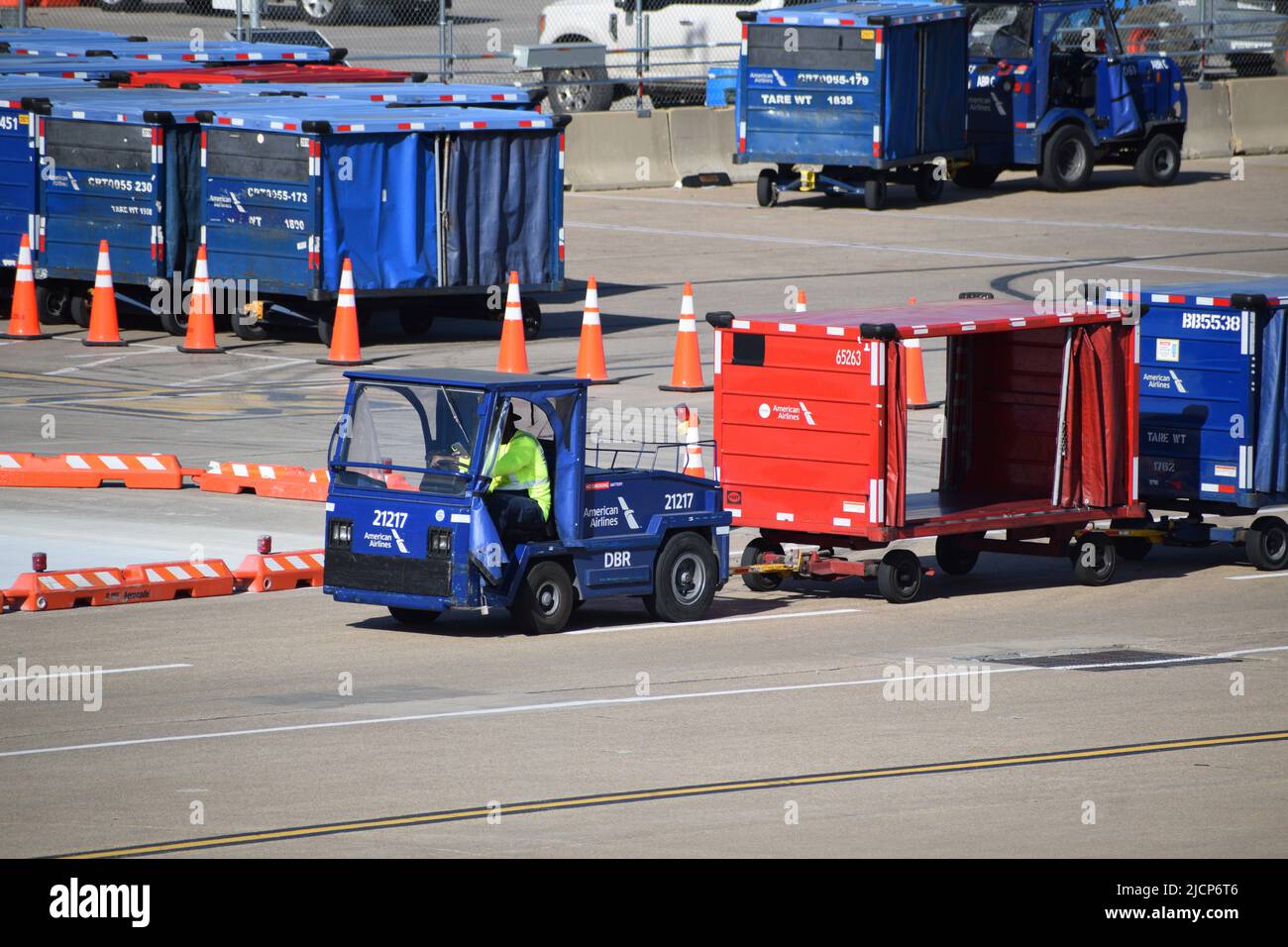 Ein Mitarbeiter der Rampendienste von American Airlines, der einen Traktor fährt, der Gepäckwagen vor Terminal C am Flughafen DFW (Dallas-Fort Worth Airport) zieht Stockfoto