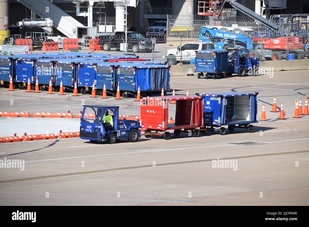 Ein Mitarbeiter der Rampendienste von American Airlines, der einen Traktor fährt, der Gepäckwagen vor Terminal C am Flughafen DFW (Dallas-Fort Worth Airport) zieht Stockfoto