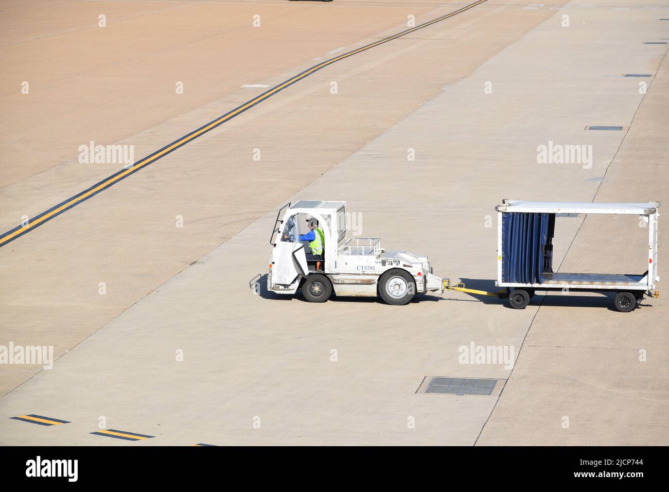 Ein Mitarbeiter von United Airlines, der einen Traktor fährt und einen leeren Gepäckwagen am Dallas Fort Worth International Airport (DFW Airport) zieht Stockfoto