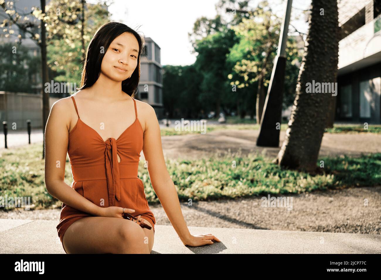 Entspannte junge asiatische Frau, die auf einer Bank in einem Stadtpark sitzt. Stockfoto
