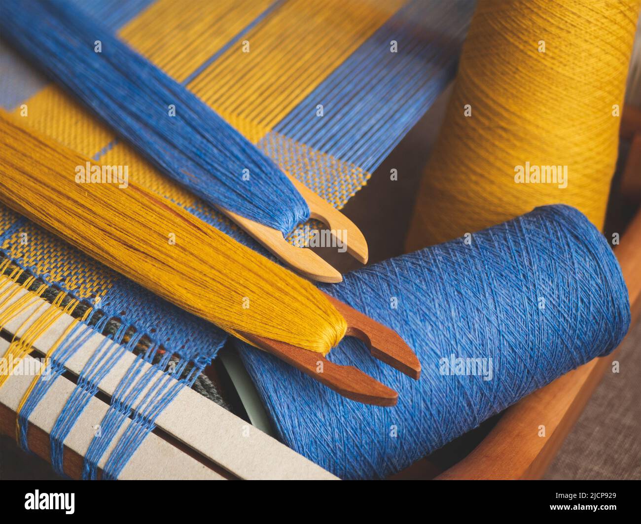 Handwebstuhl mit blau-gelber Leinwandbindung, zwei Shuttles und Garn, selektiver Fokus. Handgewebte Stoff Schöpfung in den Prozess Stockfoto
