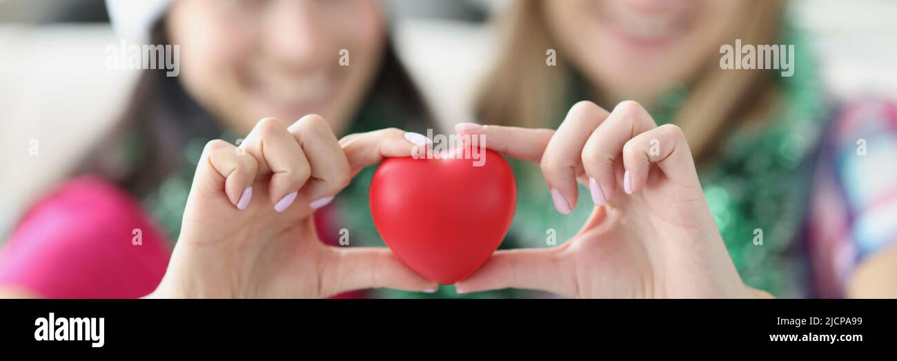 Schwestern halten rotes Herz aus Plastik in den Händen und lächeln Stockfoto
