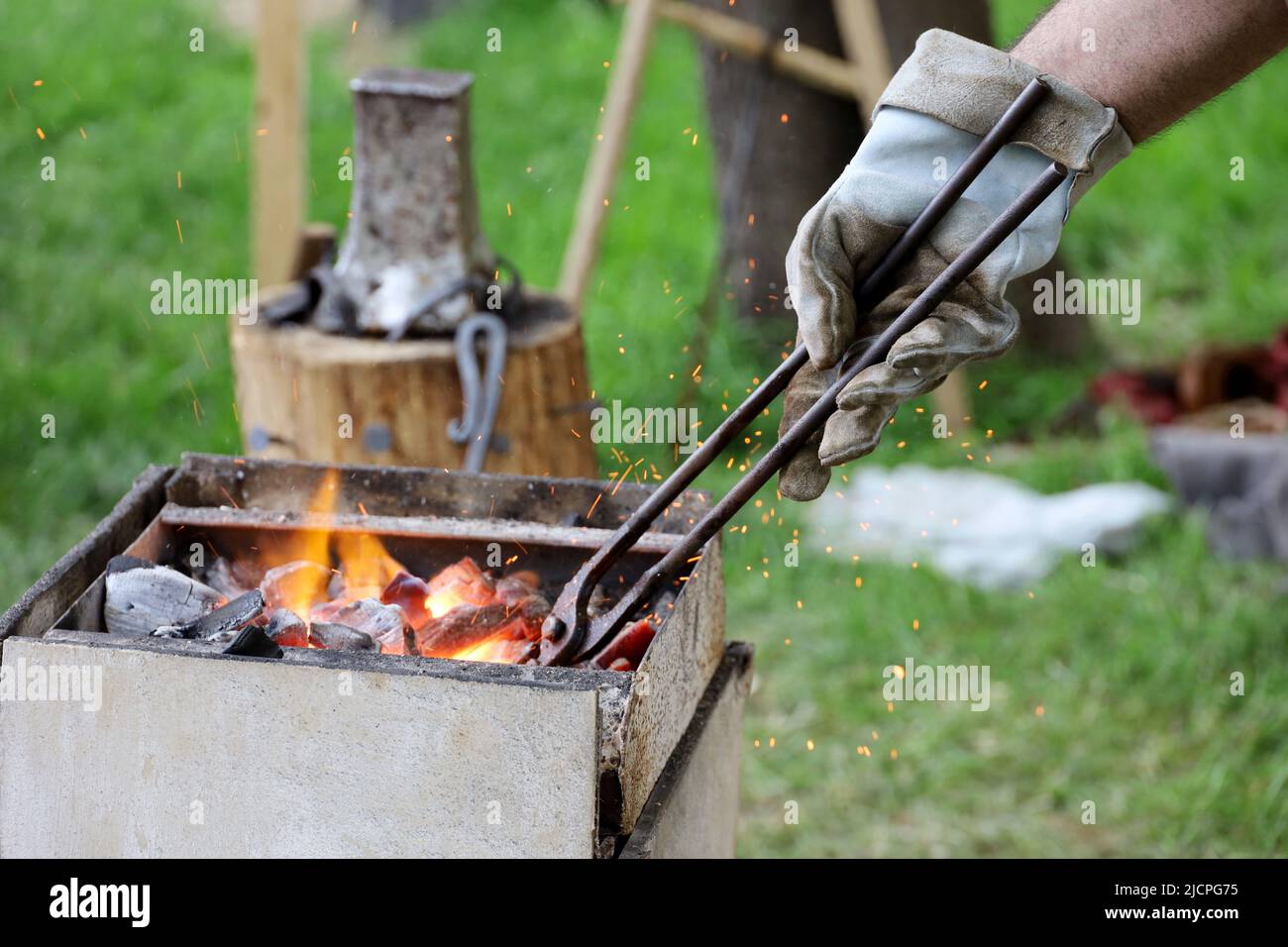 Hand des Schmieds im Handschuh mit Zecken im Feuer, Funken in einer Schmiede. Schmieden von Metallprodukten in der mittelalterlichen Schmiede Stockfoto