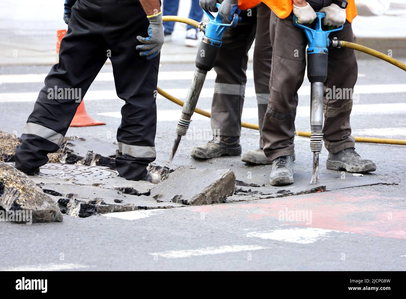 Arbeiter reparieren die Fahrbahn mit einem Presshammer. Bauarbeiten, Kanalreparatur in der Stadt Stockfoto