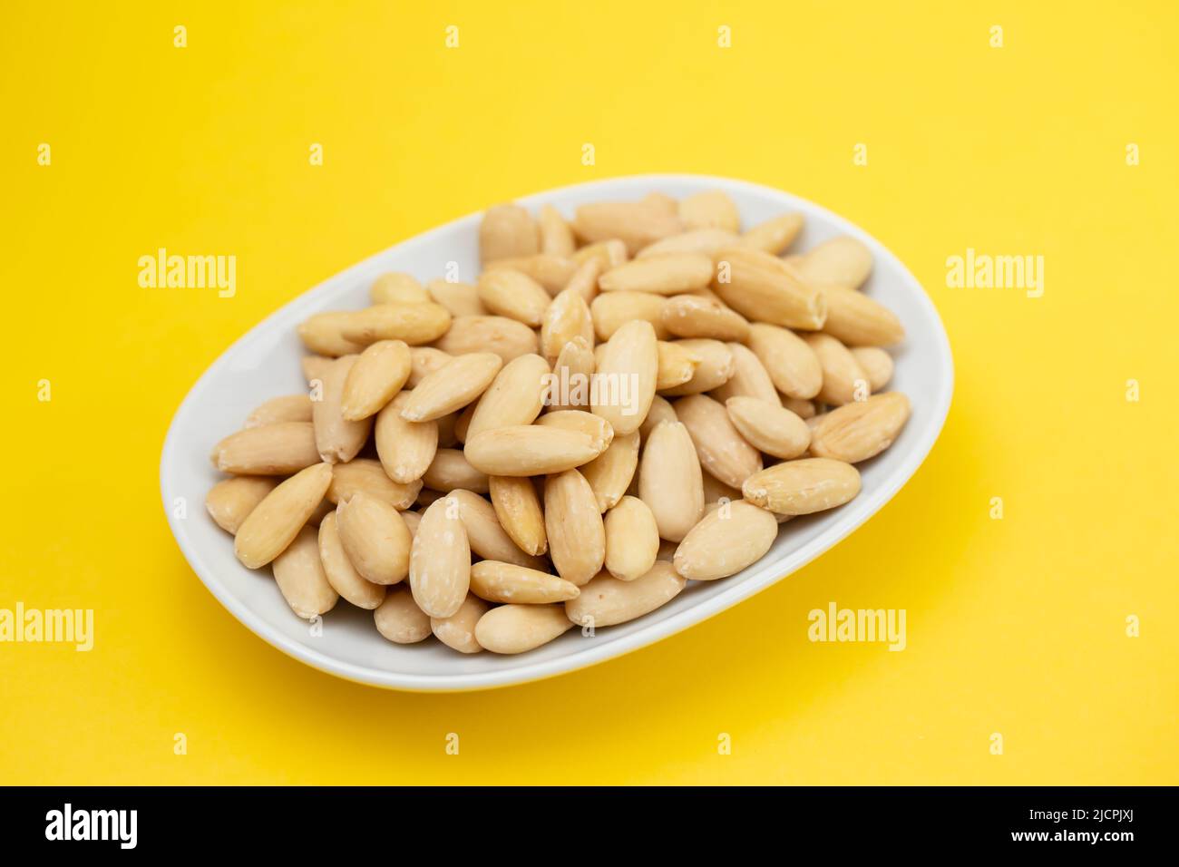 Mandeln auf einer kleinen weißen Schale auf Gelb säubern Stockfoto