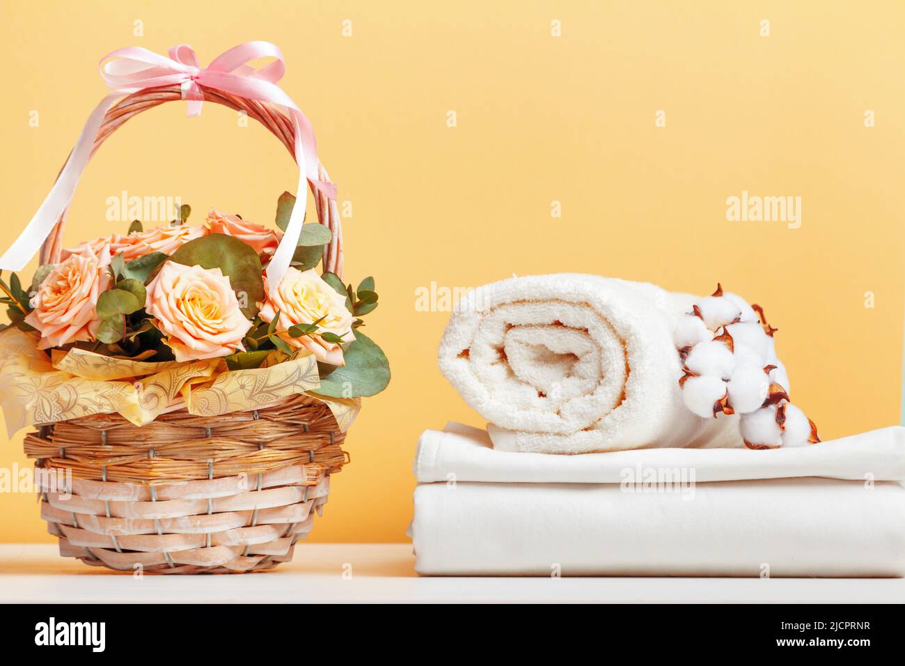 Weiße Bettwäsche, Bettwäsche und eine Rolle Handtücher. Korb mit Blumen auf dem Tisch. Stockfoto