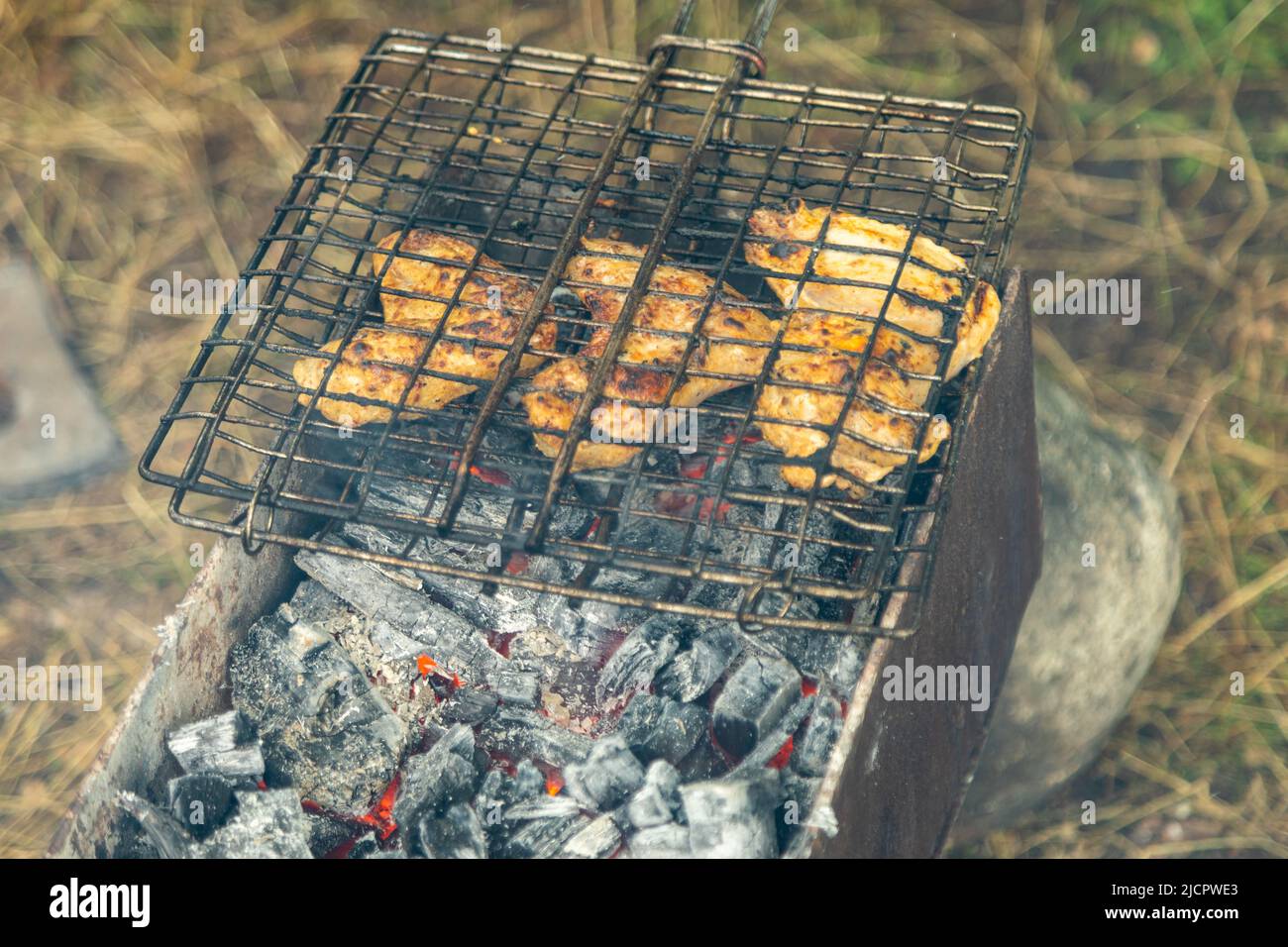 Hähnchenflügel in Metallrost grieren auf einem Brazier mit brennender Holzkohle. Grillparty im Freien Stockfoto