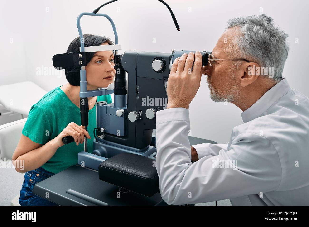 Frau bei Augenuntersuchung mit binokularer Spaltlampe in der Augenklinik mit erfahrenem grauhaarigen Optometriker Stockfoto