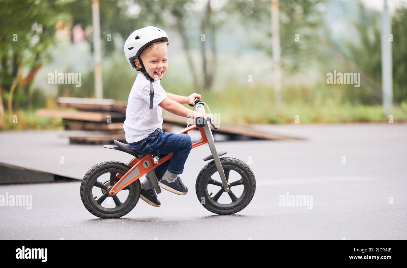Glückliches Kind Reiten Laufrad. Männliches Kleinkind im Helm, das im Skatepark lernt, auf dem Laufrad zu fahren. Stockfoto