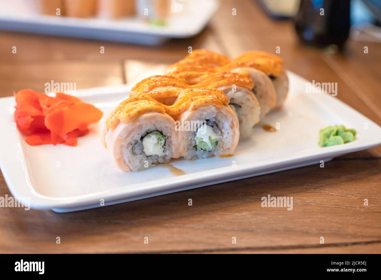 Gebackenes Maki-Sushi, gebackene Brötchen „Philadelphia“ auf weißem rechteckigem Teller. Lachs, Reis, Frischkäse, Gurken, Nori-Algen, Würzige und ungagische Saucen. Stockfoto