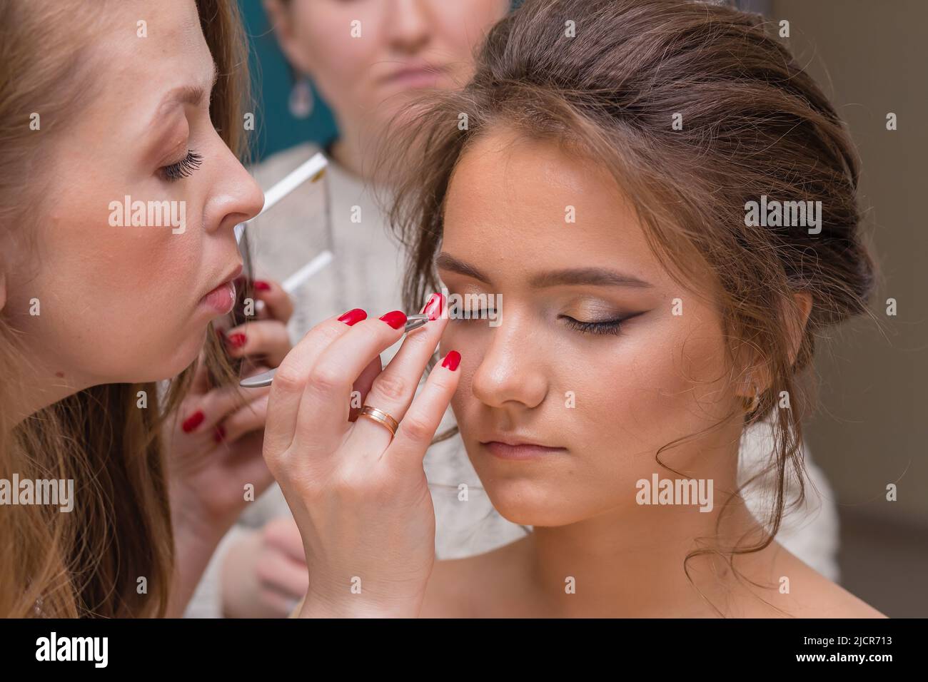 Ein professioneller Make-up-Künstler korrigiert Schatten auf dem Augenlid eines Mädchens mit einem Finger. Weibliche Meisterin macht einer jungen Frau Make-up. Geschäftskonzept - Schönheitssalon, Gesichtshautpflege, Kosmetik. Stockfoto