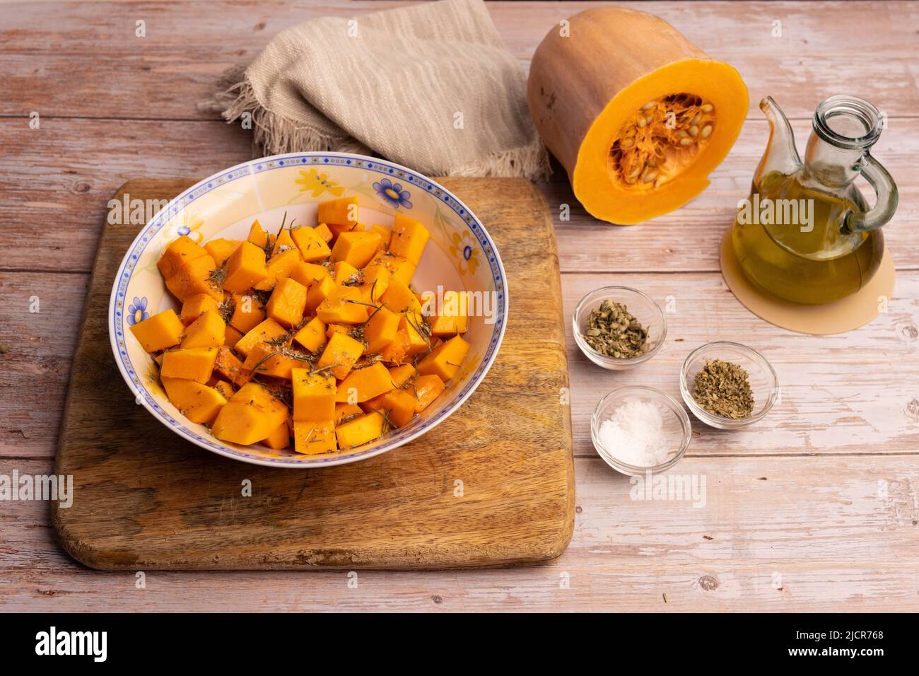 Gewürfelte Kürbisstücke in einer Schüssel, mit Gewürzen und Olivenöl Stockfoto