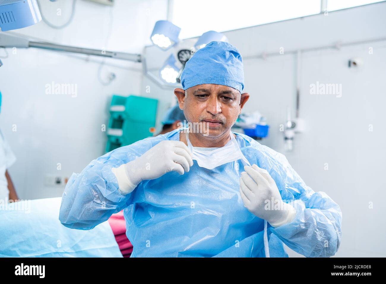 Chirurg entspannend durch Entfernen der chirurgischen Maske nach erfolgreicher Operation im OP-Theater - Konzept der Überlastung, fleißiges Arbeiten und Gesundheitsversorgung oder medizinisch Stockfoto
