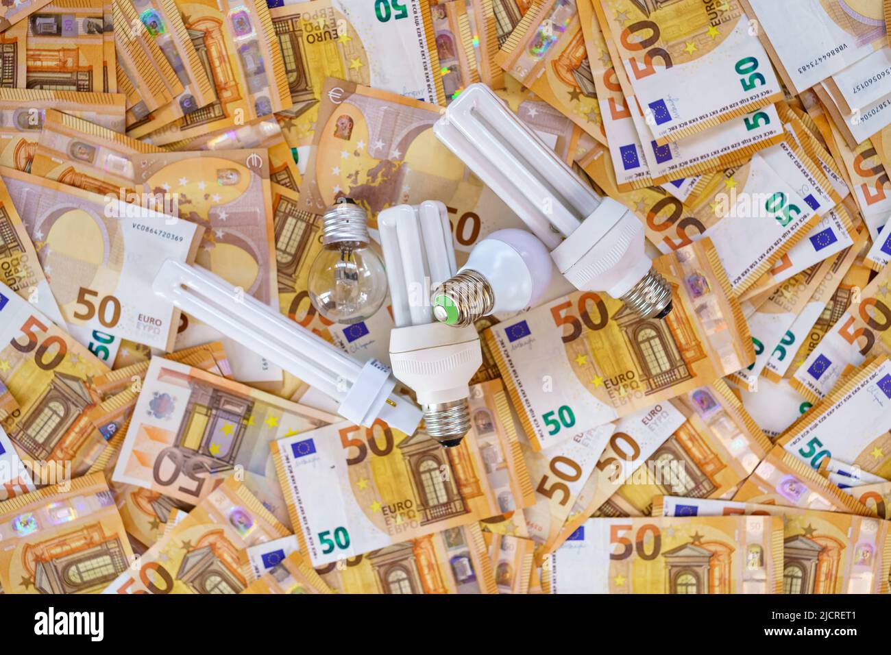 Hintergrund mit Euro-Banknoten und verschiedenen Glühbirnen, die die Stromkosten darstellen. Stockfoto
