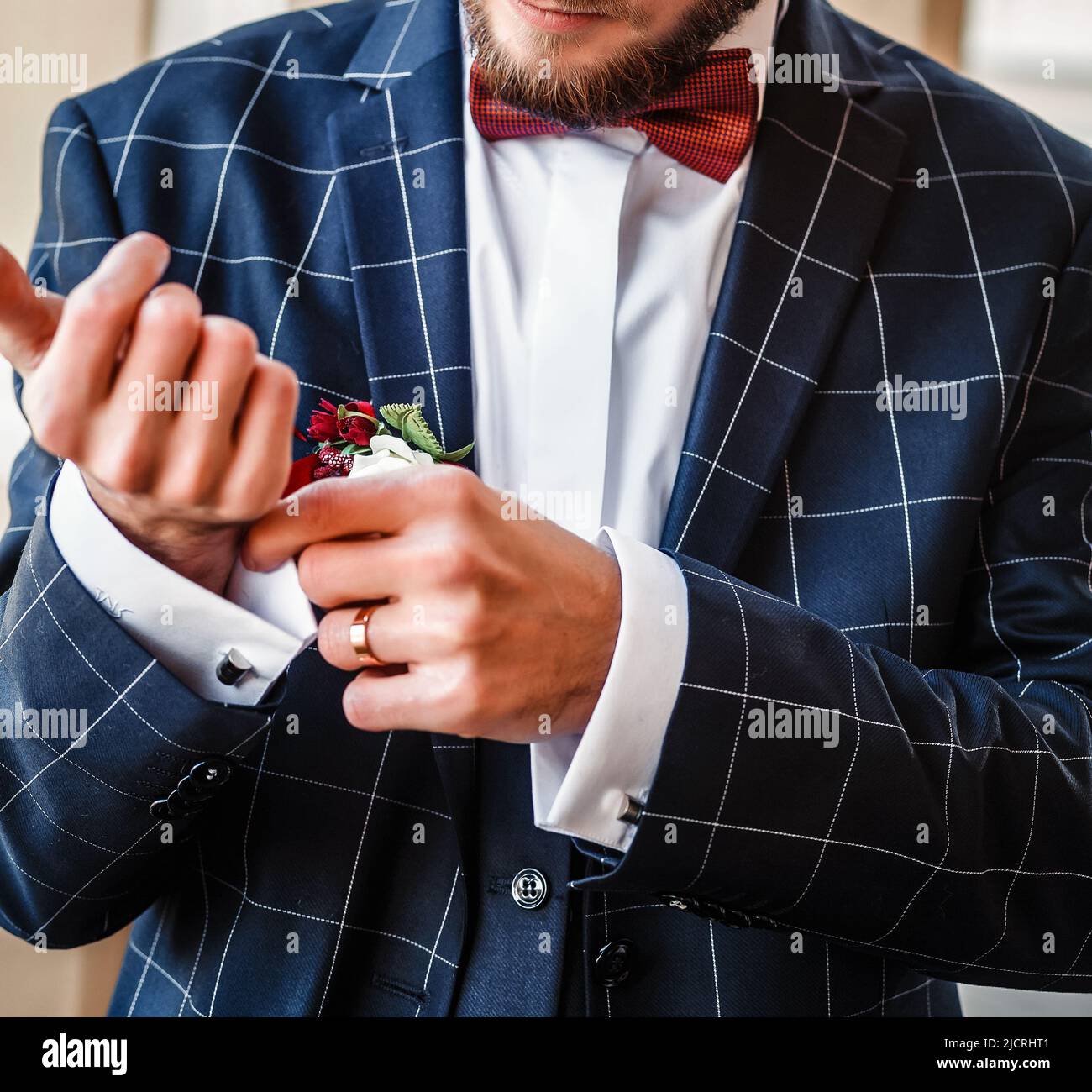 Verschwommener Hochzeitshintergrund. Ein junger Mann in einem karierten Anzug strafft seine Hemdmanschetten. Der Bräutigam in einer blauen Jacke strafft den Manschettenknauf am Ärmel Stockfoto