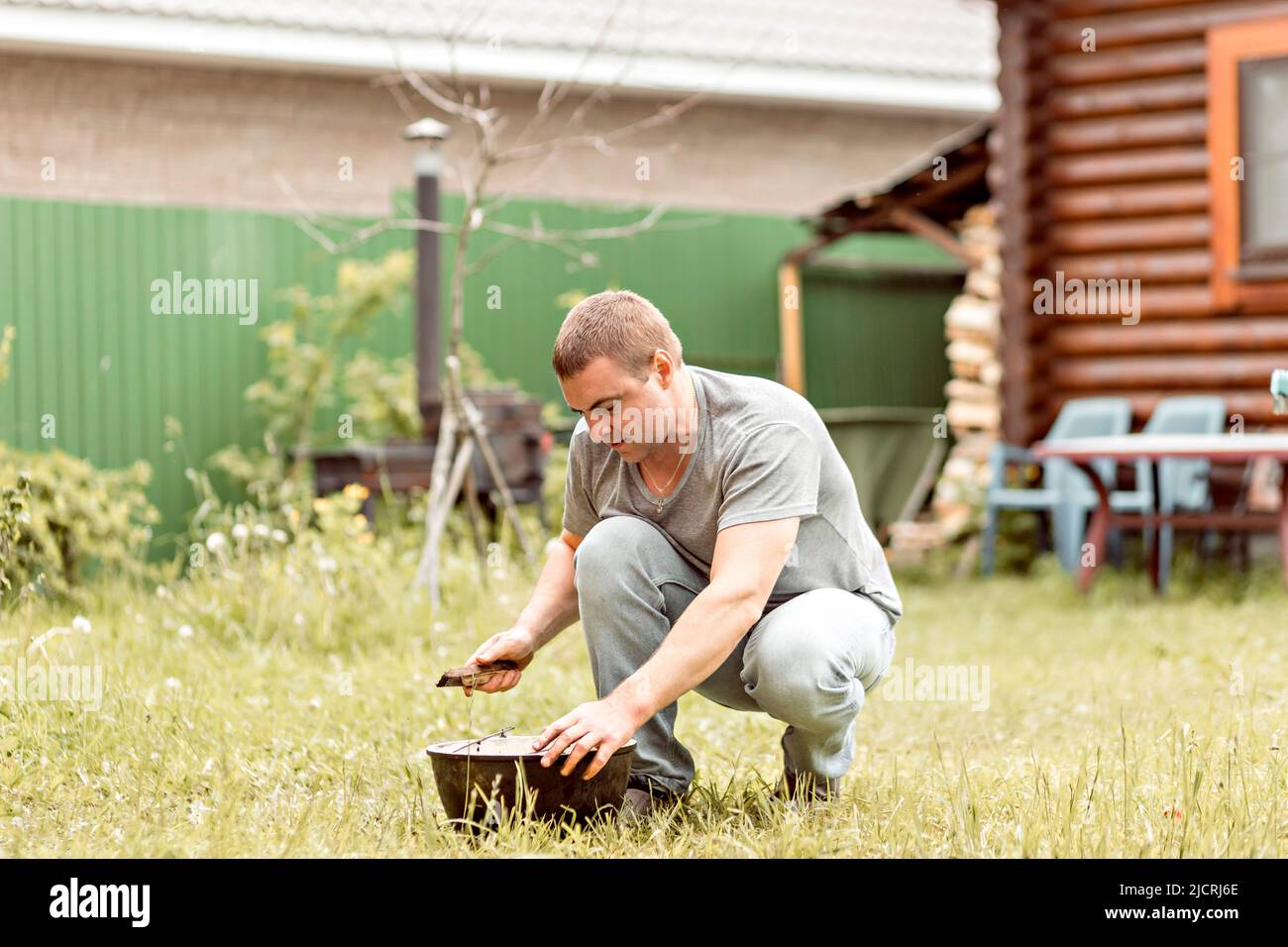 Ein Mann macht seine Hausaufgaben, reinigt einen Kessel im Hinterhof eines Landhauses. Stockfoto