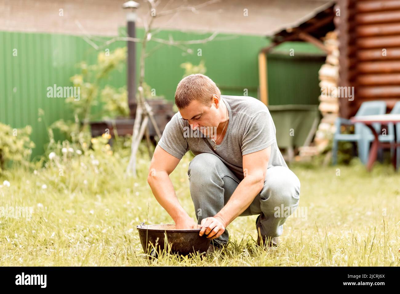 Ein Mann macht seine Hausaufgaben, reinigt einen Kessel im Hinterhof eines Landhauses. Stockfoto