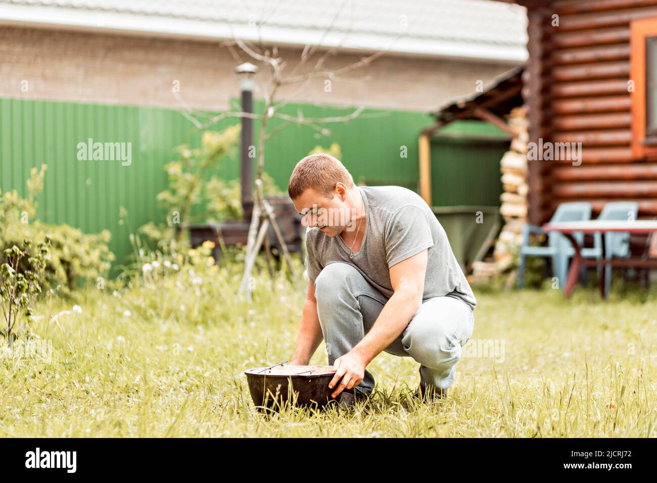 Ein Mann macht seine Hausaufgaben, reinigt einen Kessel im Hinterhof eines Landhauses. Stockfoto