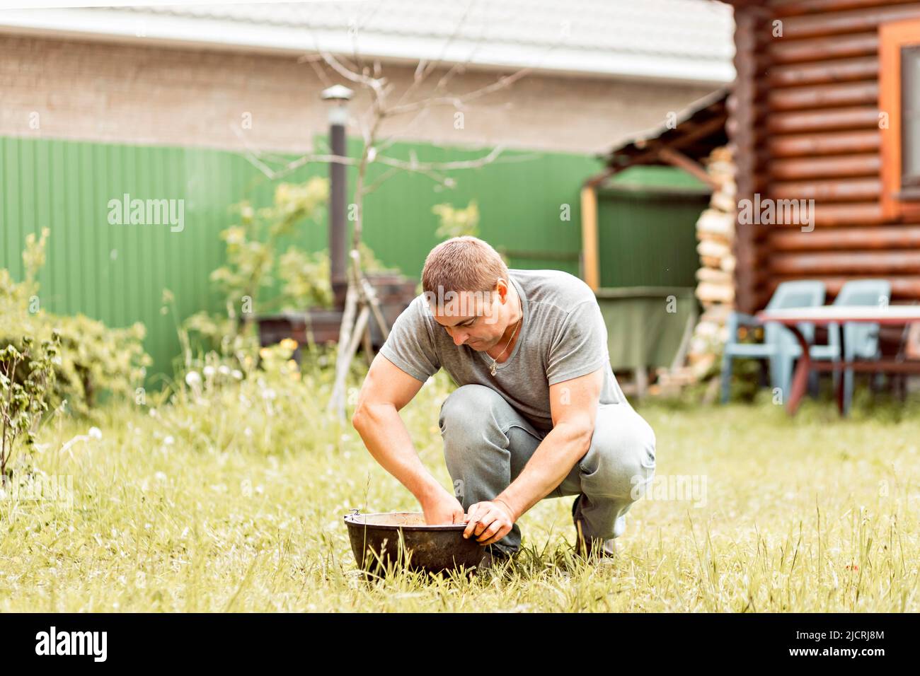 Ein Mann macht seine Hausaufgaben, reinigt einen Kessel im Hinterhof eines Landhauses. Stockfoto