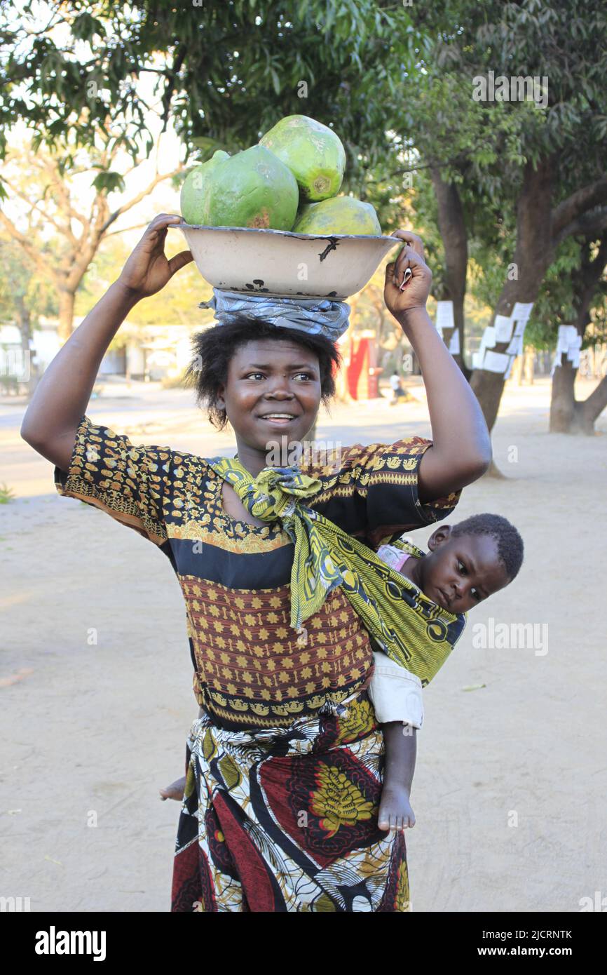Afrikanisches Leben, Dame, die Streetfood verkauft, Kind trägt Stockfoto