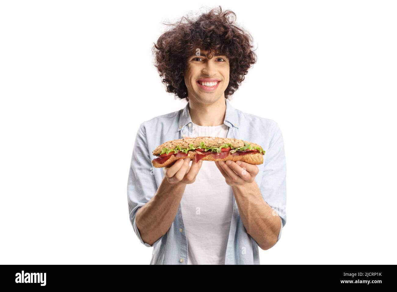 Junger Mann mit lockigen Haaren, hält ein Baguette-Sandwich und lächelt isoliert auf weißem Hintergrund Stockfoto