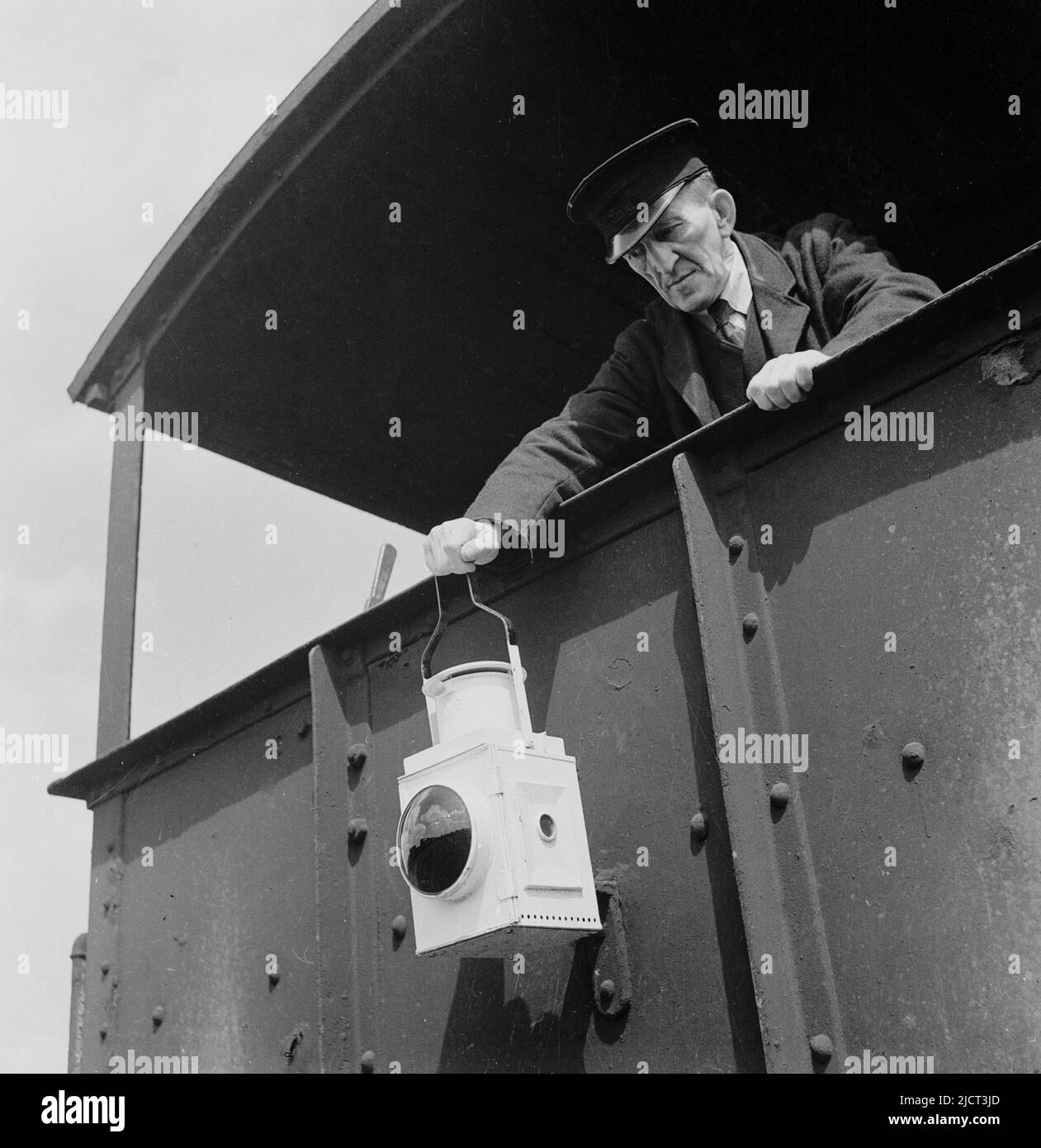 1950s, historischer, uniformierte Zugwächter, der eine Warnlaterne auf der Rückseite eines Güterwagens der Great Western Railways befestigt, Docks in London, London, England, Großbritannien. Stockfoto