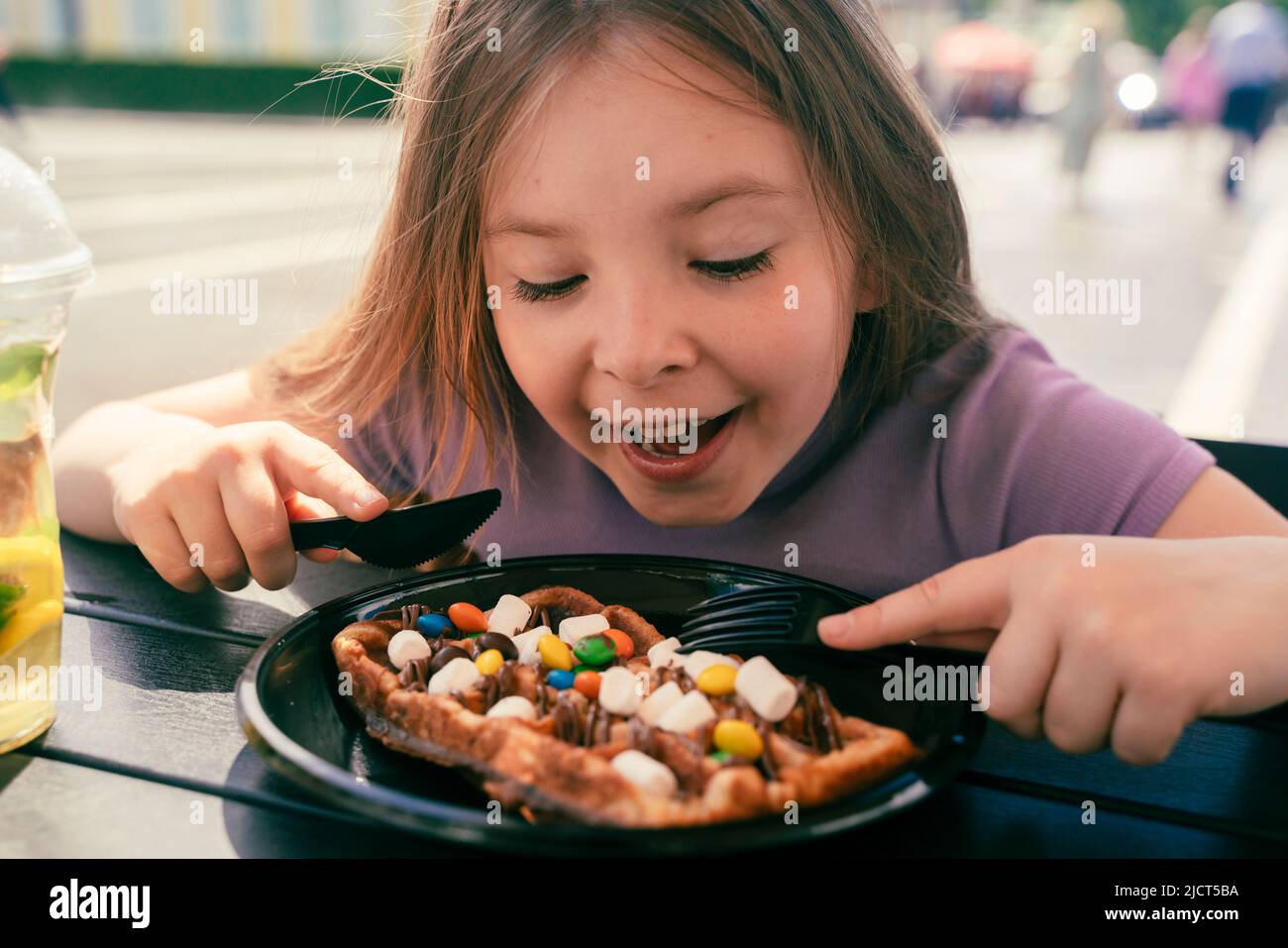 Ein 8-jähriges Mädchen isst in einem Straßencafé eine Wiener Waffel. Hochwertige Fotos Stockfoto