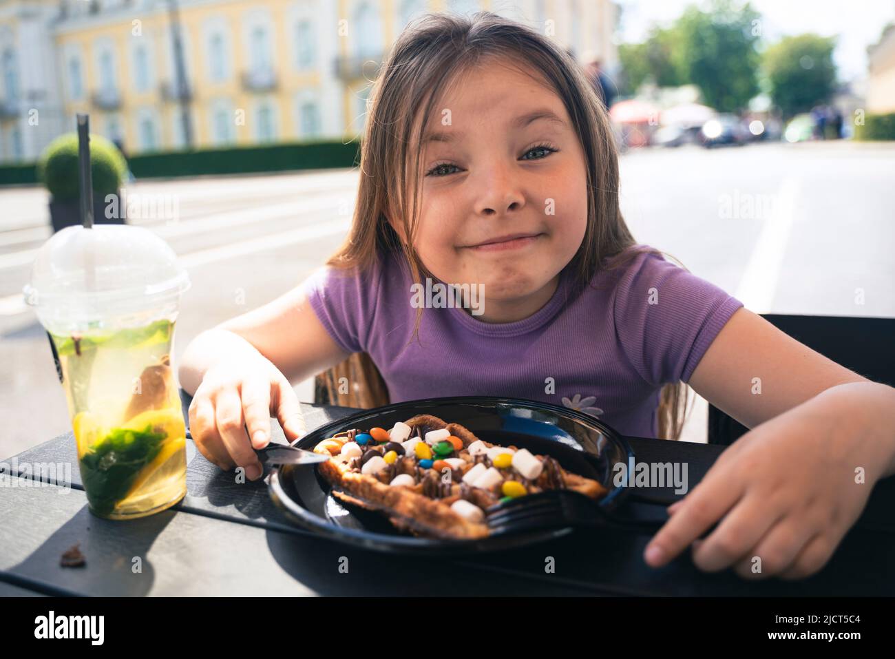 Ein 8-jähriges Mädchen isst in einem Straßencafé eine Wiener Waffel. Hochwertige Fotos Stockfoto