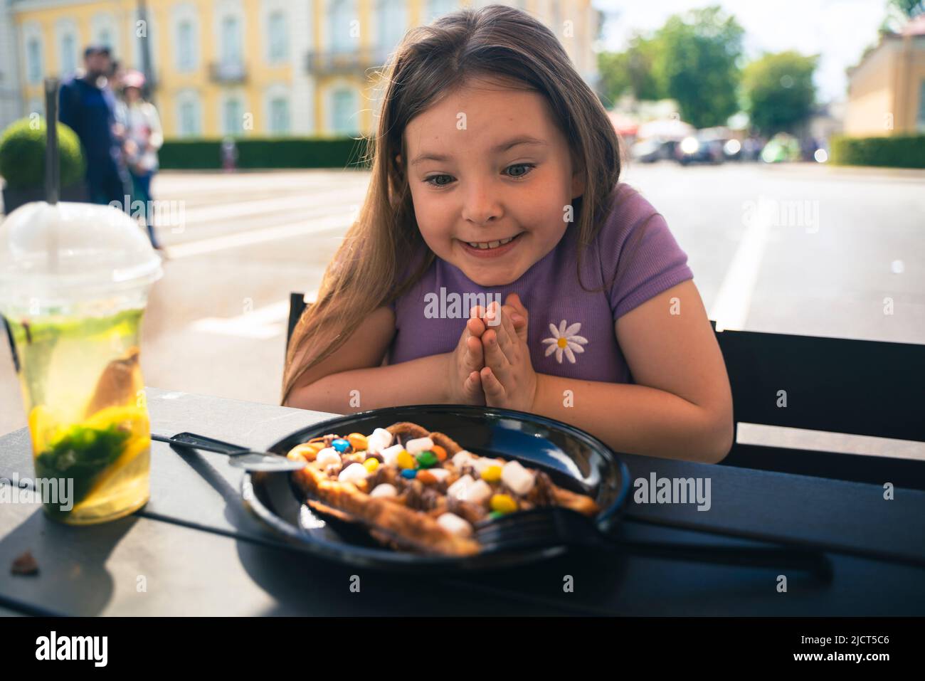 Ein 8-jähriges Mädchen isst in einem Straßencafé eine Wiener Waffel. Hochwertige Fotos Stockfoto