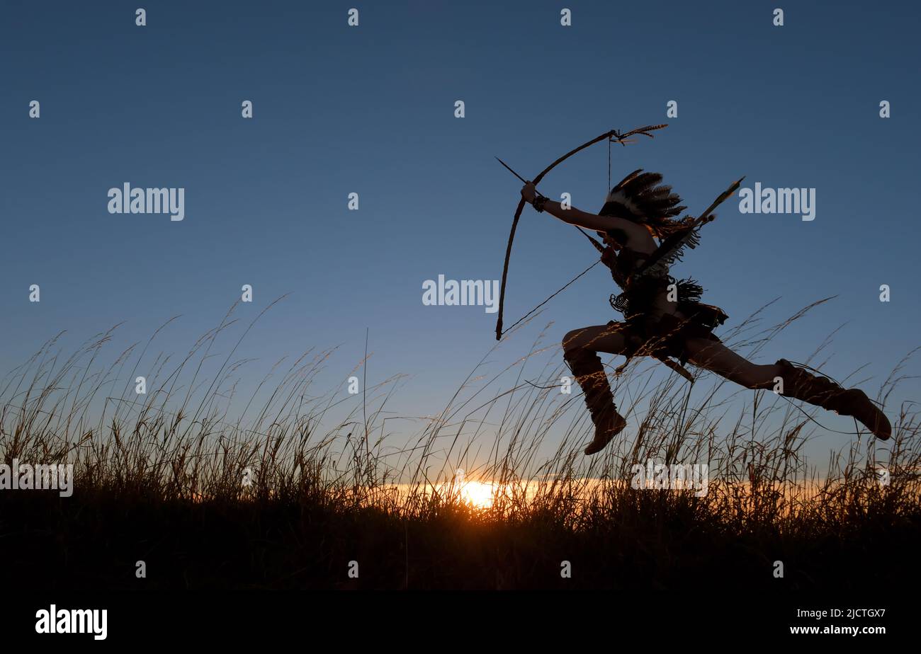 Ein indianisches Mädchen der Ureinwohner wird bei Sonnenuntergang durch das Grasland Rennen und Rennen sehen. Sie springt hoch und hält ihre Waffen an ihrer Seite Stockfoto