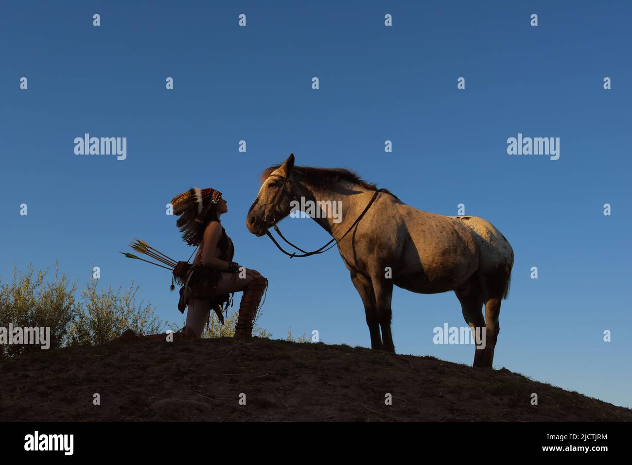 Ein junges Mädchen wird bei Sonnenuntergang als Indianerin der Ureinwohner Amerikas gesehen. Sie hält auf einem kleinen Hügel inne, um ihr Pferd zu schätzen Stockfoto