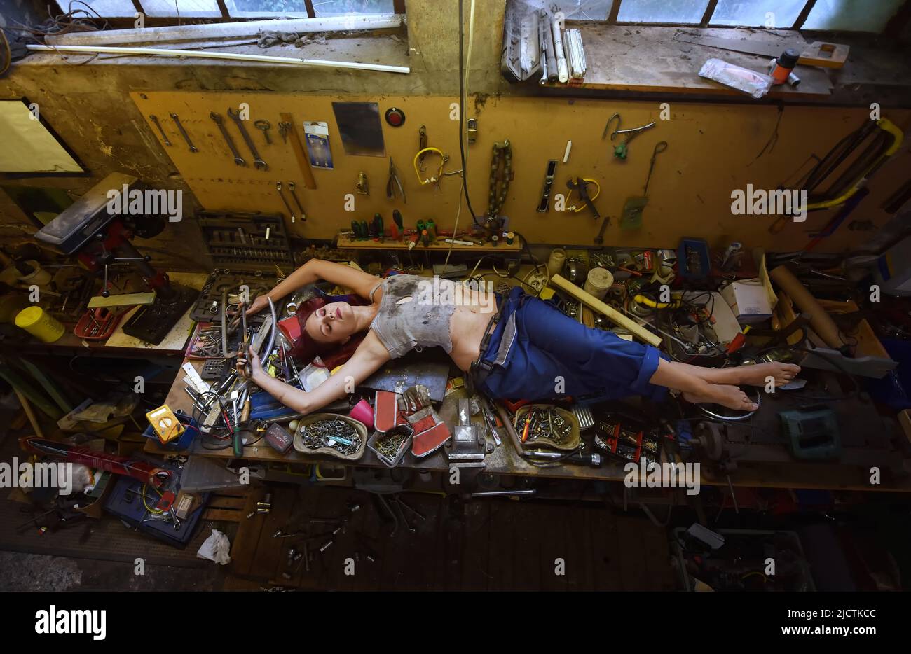 Eine junge, schöne Frau findet während ihrer Arbeitszeit Zeit zum Schlafen. Sie legt sich auf den Arbeitstisch, der mit Werkzeugen und anderen elektronischen Geräten gefüllt ist. Stockfoto