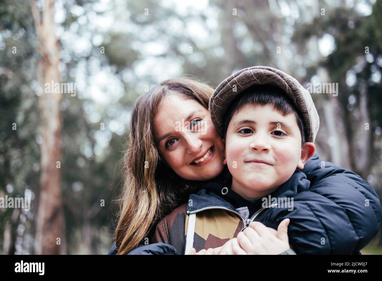 Die junge blonde lateinische Mutter umarmt ihren jungen Sohn im Park. Alleinerziehende Familie Stockfoto