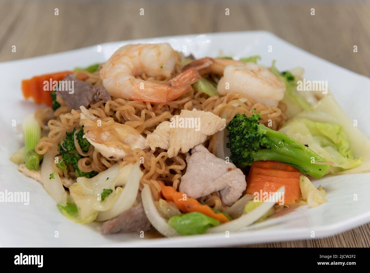 Herzhafte Teller mit Chow mein gekrönt mit großen Garnelen, gegrilltem Gemüse und verzehrfertig. Stockfoto