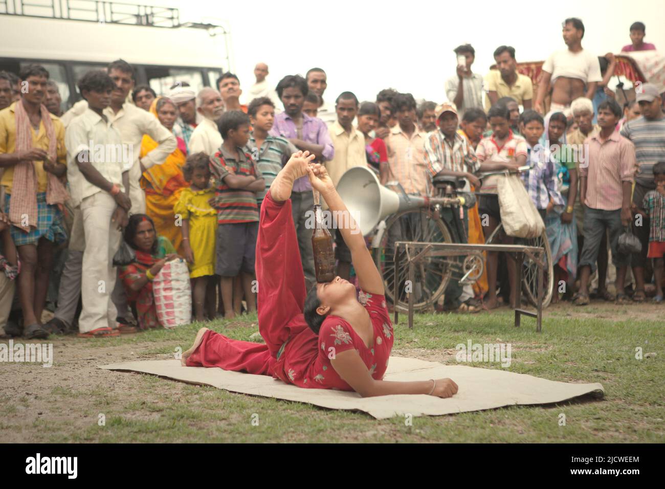 Eine Frau, die vor Dutzenden von Zuschauern auf einem Feld am Straßenrand am Stadtrand von Rajgir in Bihar, Indien, einen Gymnastikstunt mit einer Flasche vorführt. Stockfoto