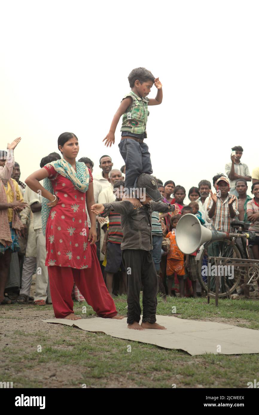 Kinder, die vor Dutzenden von Zuschauern auf einem Feld am Straßenrand am Stadtrand von Rajgir in Bihar, Indien, einen Gymnastikstunt durchführen. Stockfoto