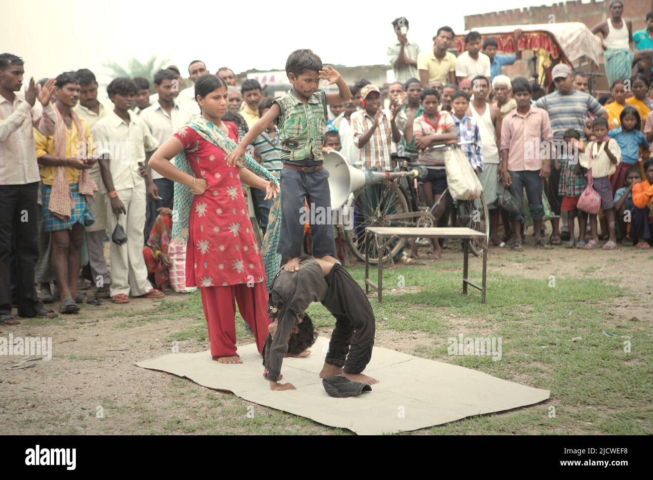 Kinder, die vor Dutzenden von Zuschauern auf einem Feld am Straßenrand am Stadtrand von Rajgir in Bihar, Indien, einen Gymnastikstunt durchführen. Stockfoto