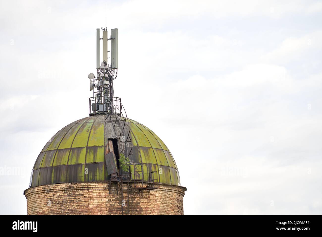 Ein alter Ziegelturm mit verwittertem Metalldach und Funkantenne Sender gegen bewölkten Himmel und. Internet-, 3G-, 4G- und 5G-Mobilfunkverbindung. Stockfoto